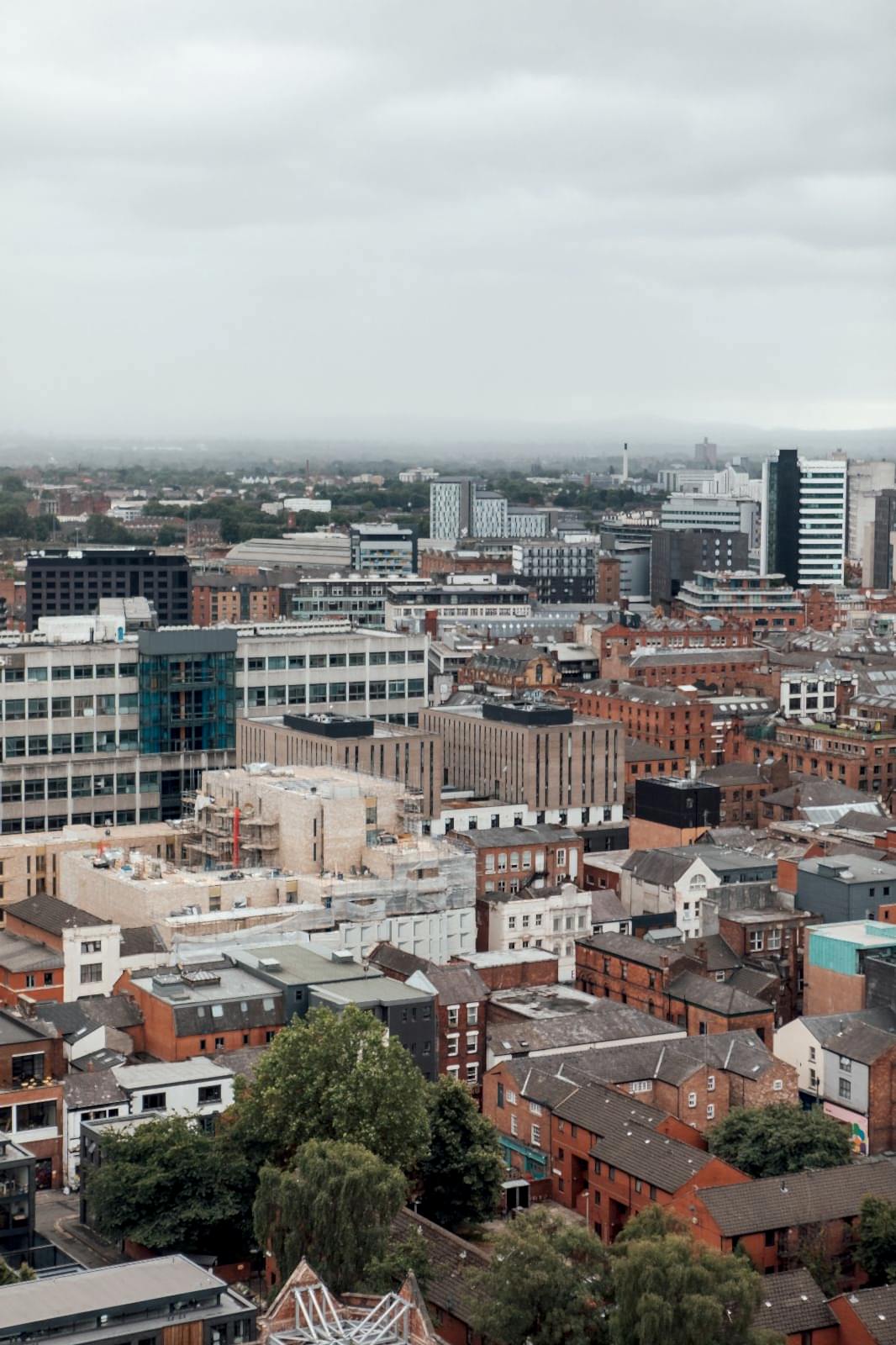 View from Swan Street House over Manchester, red brick buildings and trees. Soft grey daytime lighting.