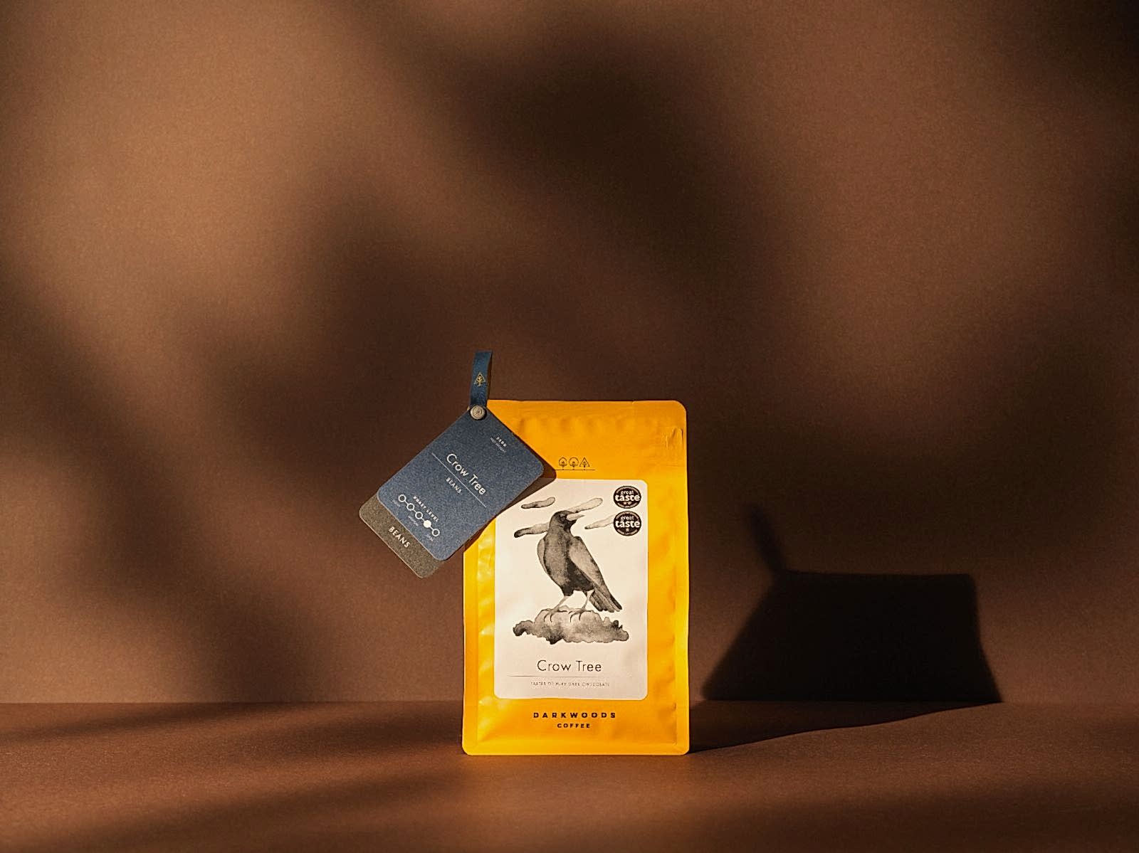 Dark woods coffee - Yellow Crow Tree packaging, with branding by 93 on dark brown background - warm studio lighting