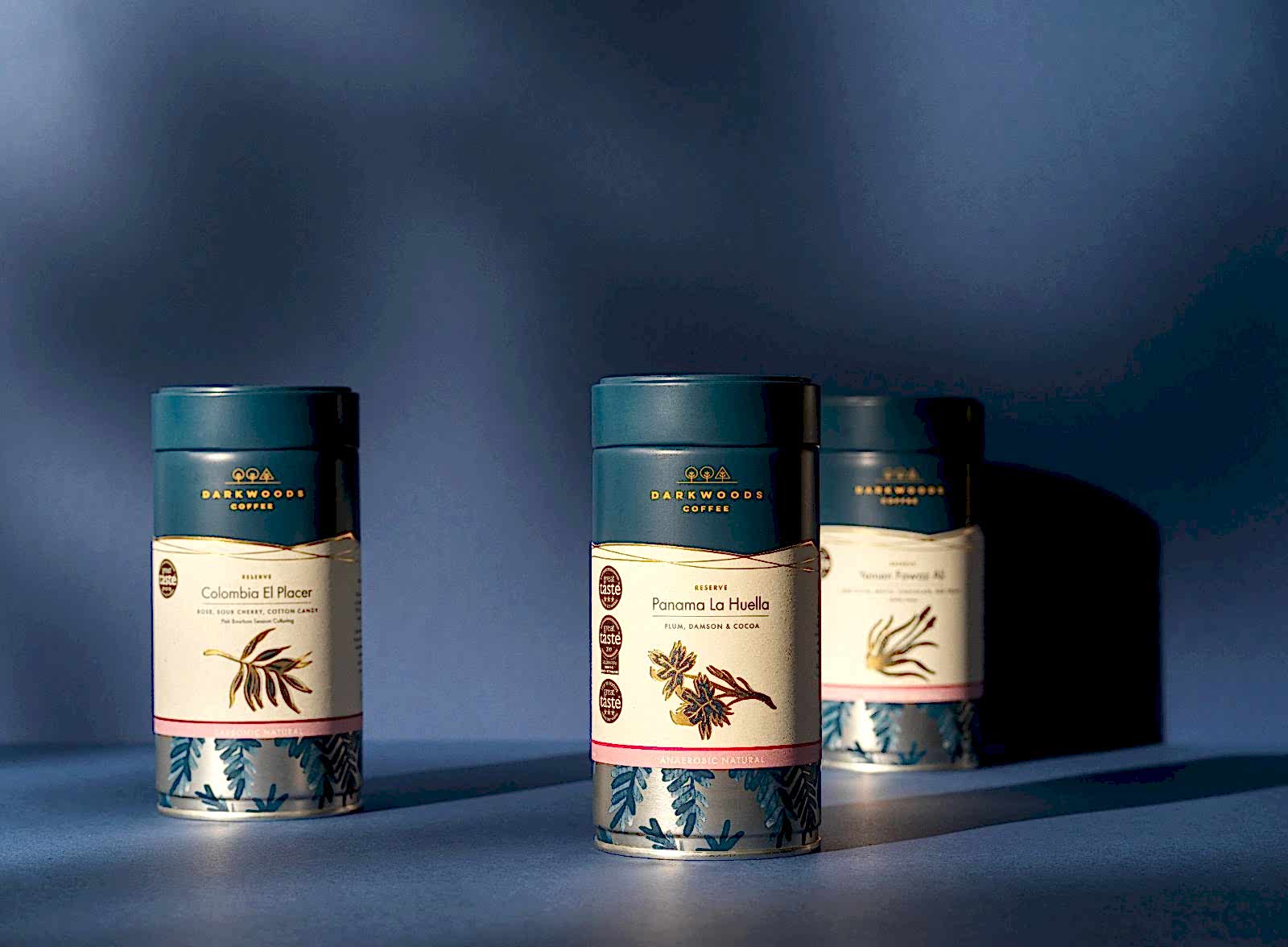 Three blue tins of Dark woods Reserve coffee on blue studio, still life background. Colombia El Placer, Panama La Huella