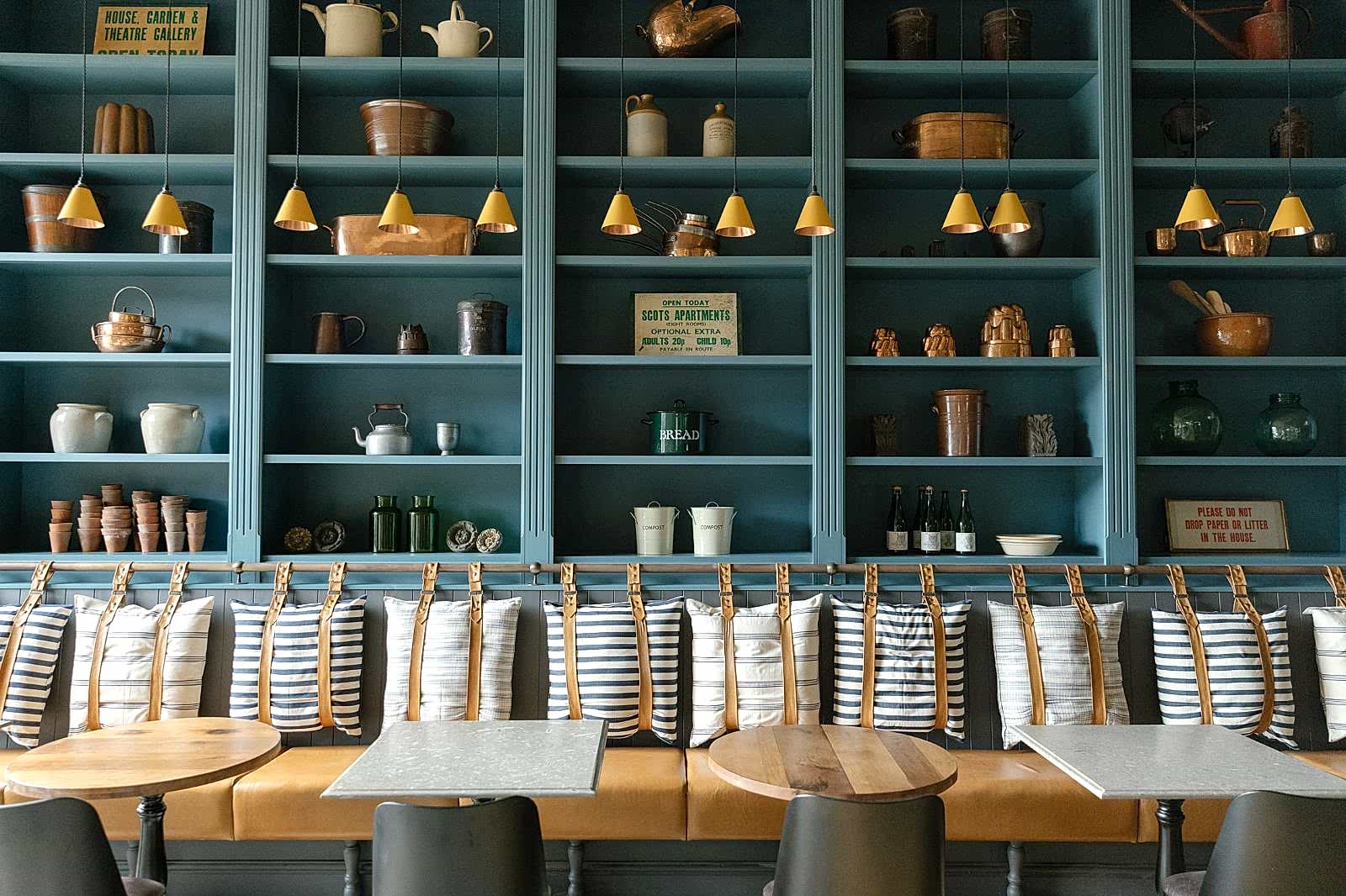 Long cushioned bench seat with four small tables in front. Blue shelving with vintage kitchenalia rises behind the bench.