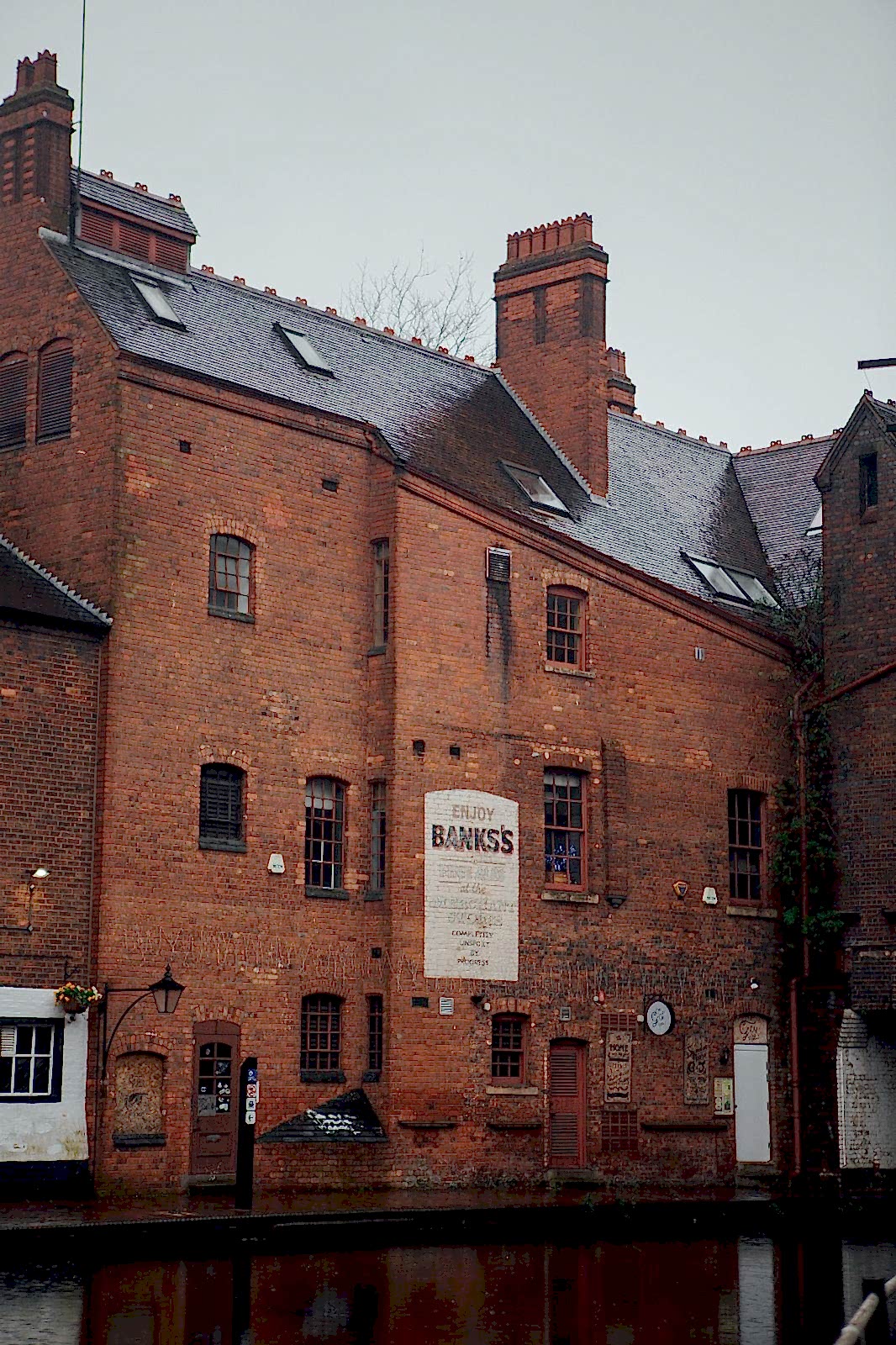 Tall Victorian red-brick building, with painted sign advertising ales, along a Birmingham canal on a rainy winterâ€™s day.