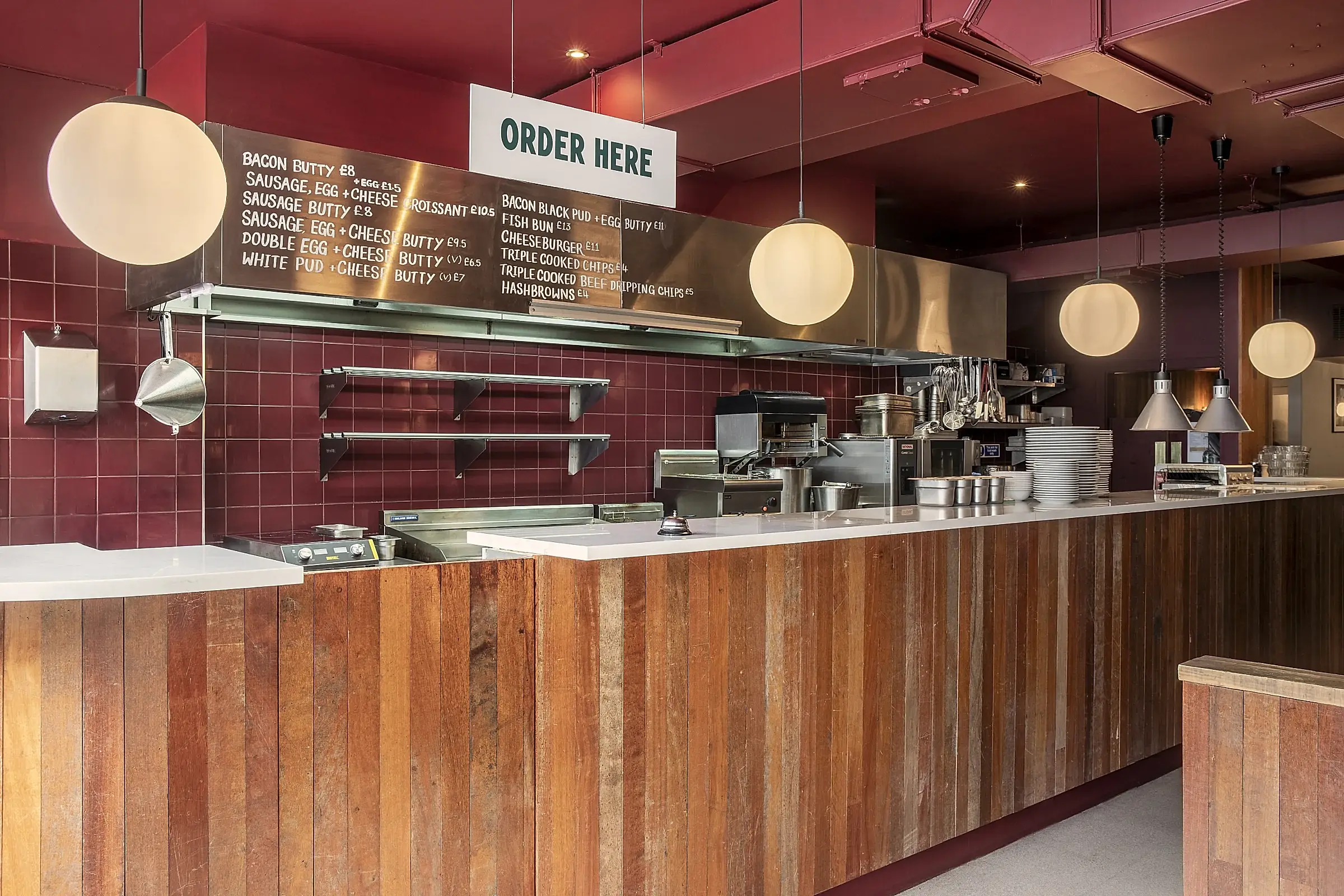 Ordering counter. Wood cladding bar with stone counter top, circular lights, and stainless steel menu board.