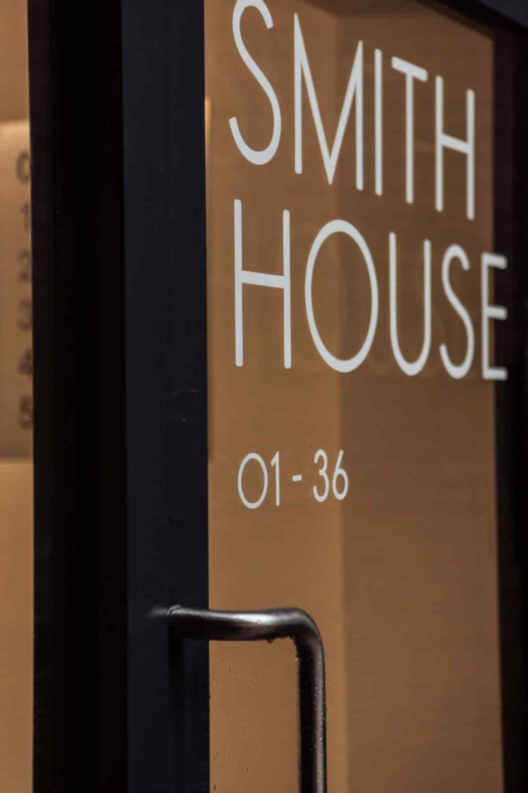 Contemporary glass entrance door with black frame and hand painted letters reading SMITH HOUSE 01-36.