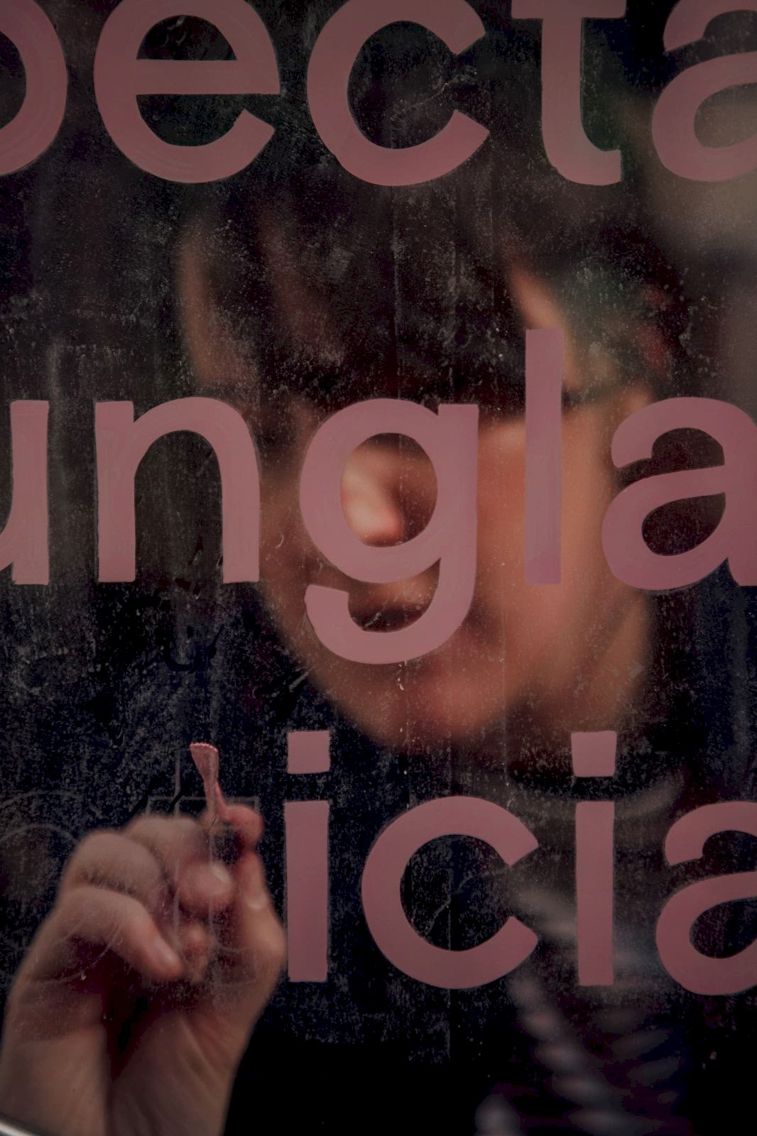 Signwriter painting pink letters on the glass window of Seen opticians shop front in Manchester. 