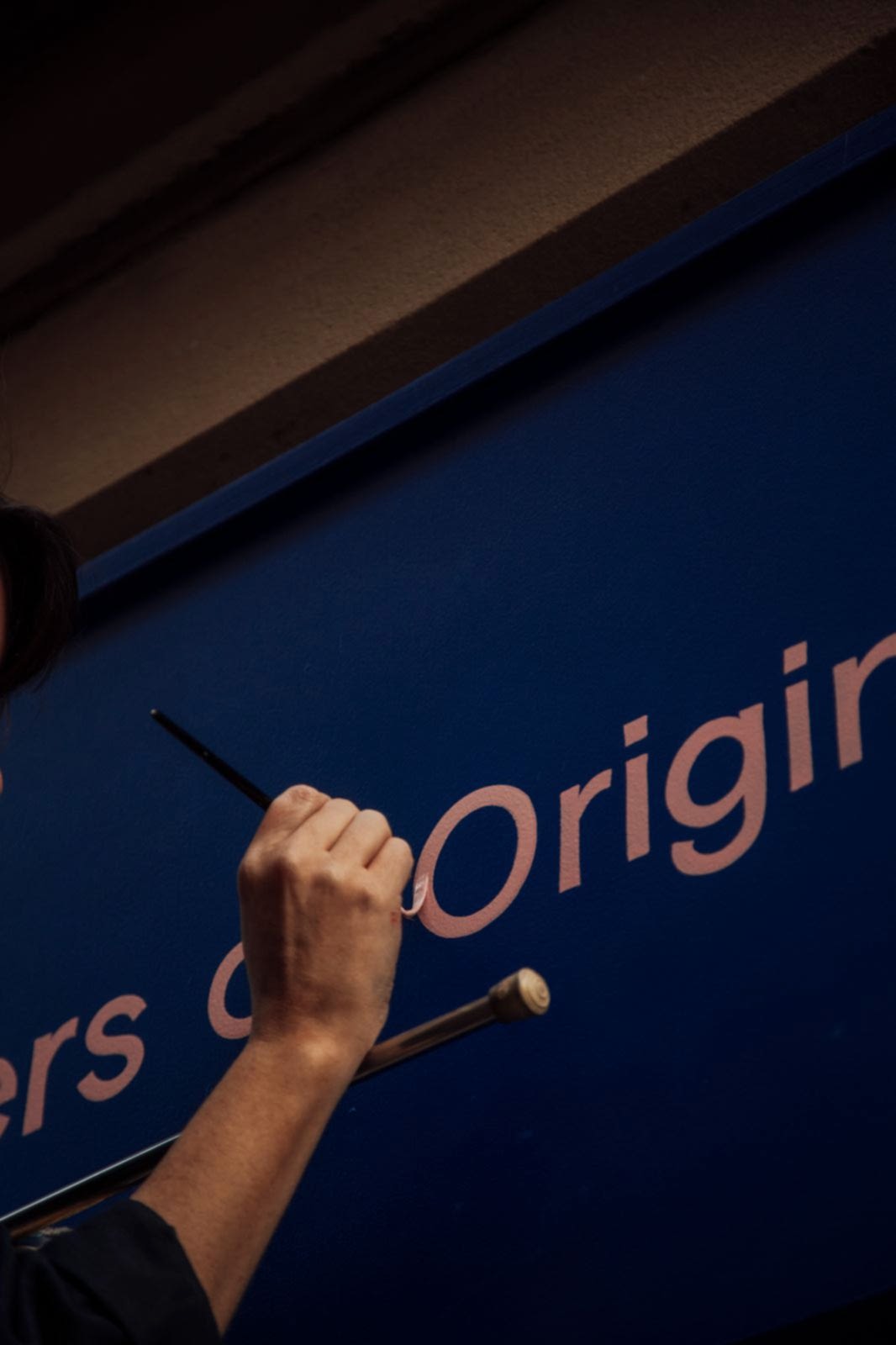 Signwriter on a ladder painting pink letters on a royal blue shop facia of an elegant stone building in Manchester