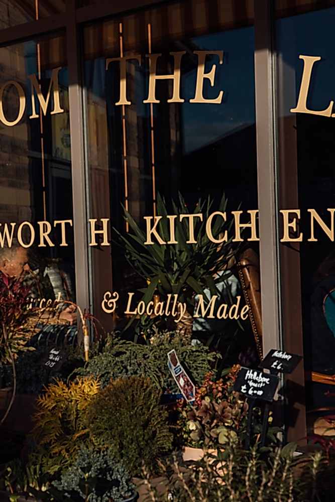 Close up of sign writing on Chatsworth Kitchen window. LOCALLY MADE. Flowers are for sale in the foreground. 