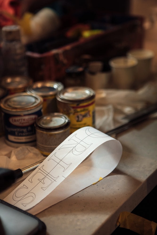 Folded sheet of paper printed with type stencil surrounded by tips of signwriting paint on a table. 