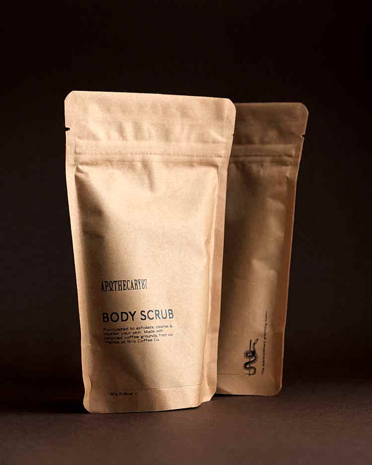 Two brown kraft paper packets of Apothecary 87 Body Scrub - branding and packaging design by 93ft Design. 