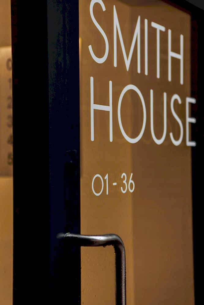 Contemporary glass entrance door with black frame and hand painted letters reading SMITH HOUSE 01-36.