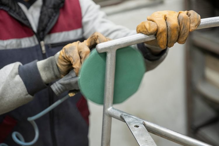 Parla metal chair frame being sanded with electric sander in a workshop - preparation for Physical Vapour Deposition