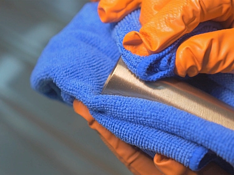 Metal tube coated with golden Physical Vapour Deposition coating being cleaned with a blue micro-cloth