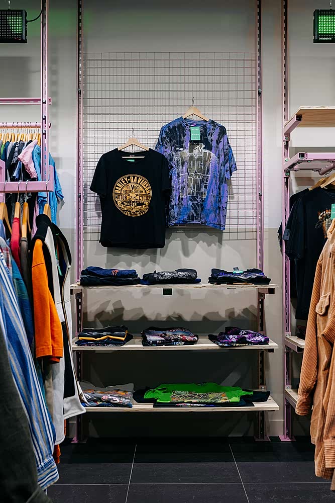 Pink unistrut industrial-style shelving unit & plywood shelves to display vintage clothing. T-shirts hanging from metal mesh