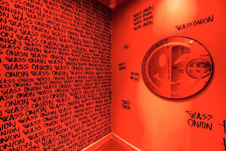 Red changing room with circular mirror with smiley face design & wallpaper repeating the words GLASS ONION