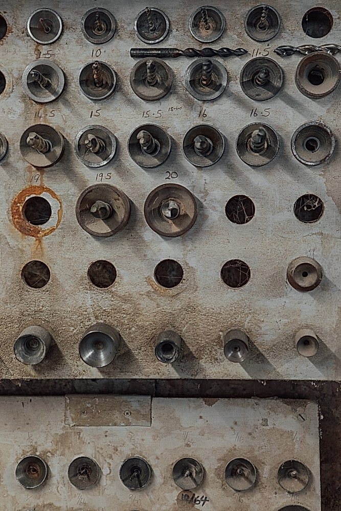 Wooden board with rows of different size drill bits, each with size number written in pencil above.