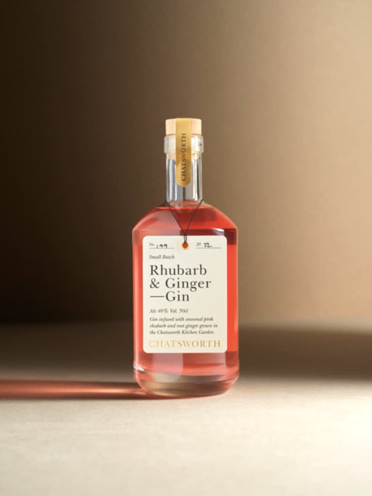 A bottle of pink small batch Chatsworth Rhubarb & Ginger Gin. Clear glass with a cork stopper, gold sticker and cream label.