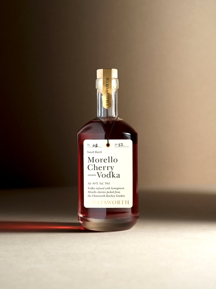 A bottle of red small batch Chatsworth Damson Gin. Clear glass with a cork stopper, gold sticker and cream label.